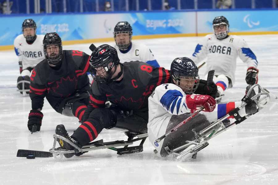 South Korea's Choi Kwang-hyuk, right, battles for the puck against Tyler McGregor of Canada during they para ice hockey preliminary match at the 2022 Winter Paralympics, Tuesday, March 8, 2022, in Beijing.