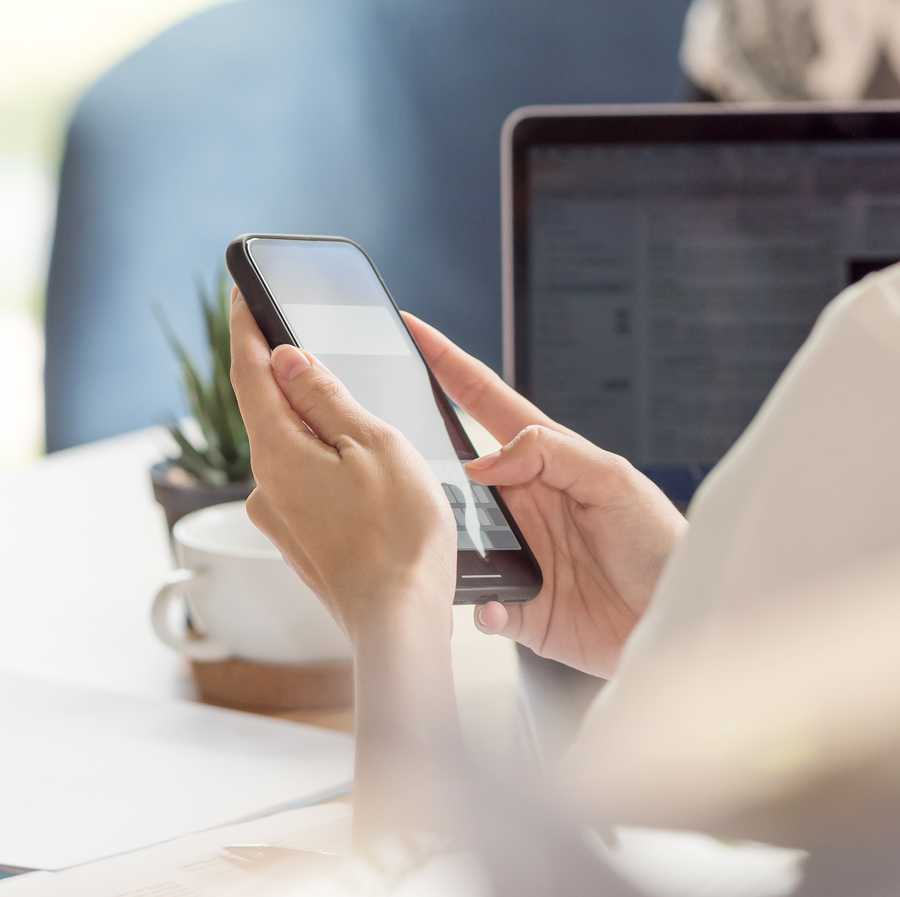 Female hand using smartphone while working at desk in office