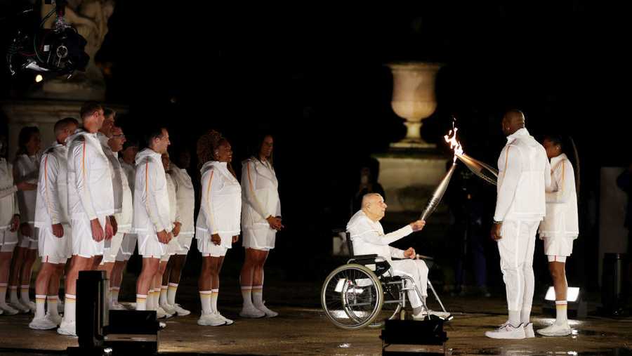 PARIS, FRANCE - JULY 26: Torch bearer Charles Coste passes the torch to French Athlete Marie-Jose Perec and French Judo Practitioner Teddy Riner walk to light the Olympic Cauldron at the Gardens of the Tuileries during the opening ceremony of the Olympic Games Paris 2024 on July 26, 2024 in Paris, France. (Photo by Al Bello/Getty Images)