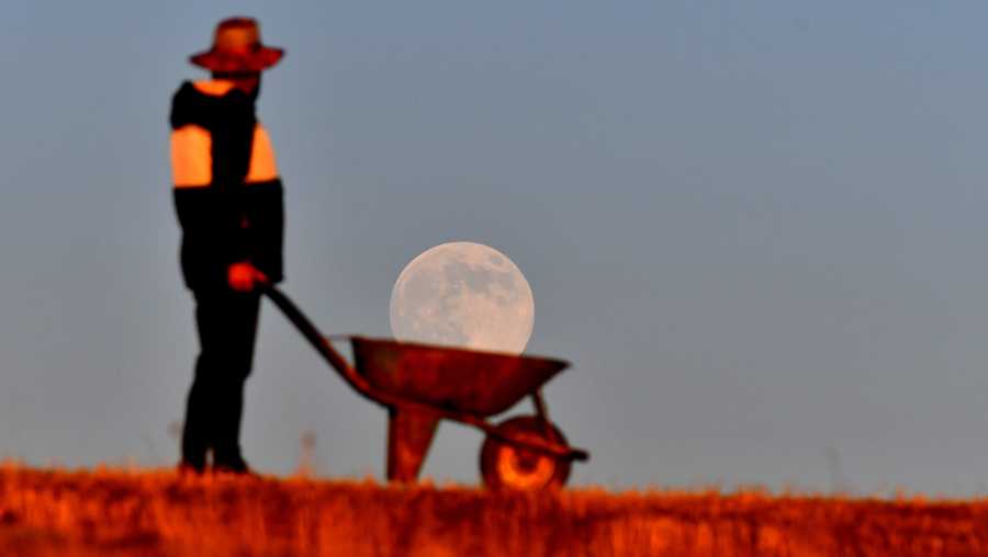 KARS, TURKIYE - DECEMBER 4: A man poses for a photo as if he is carrying the full moon in a wheelbarrow while it rises behind the horizon in Sarikamis district of Kars, Turkiye on December 4, 2025. (Photo by Huseyin Demirci/Anadolu via Getty Images)